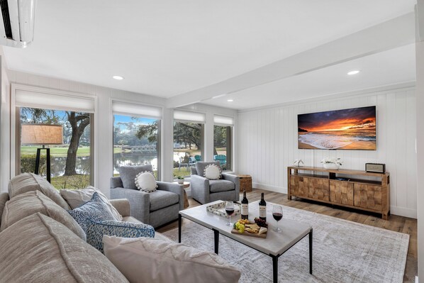 Amplia sala de estar con televisor grande, asientos cómodos, un mueble de madera y vistas al exterior.