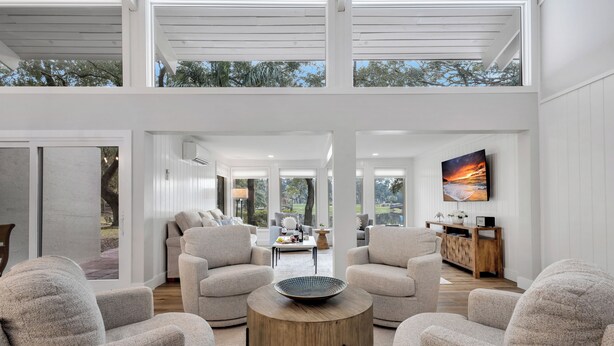 A modern living room with a round wooden coffee table, beige armchairs, and a large painting on the wall.