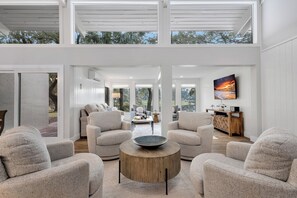 Una sala de estar moderna con una mesa redonda de madera, sillones color beige y un cuadro grande en la pared.