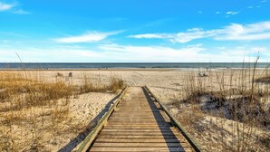 A wooden boardwalk leading to a beach with sand dunes and sparse vegetation.