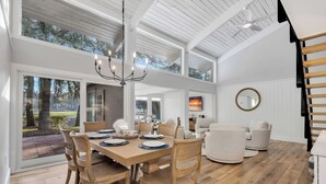 A spacious dining area with a wooden table and chairs, large windows, and a view of the outdoors.