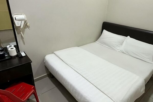 A hotel room with a bed, a desk with a mirror, a red chair, and a hairdryer on the wall. - Hotel Lean Fatt (Ipoh)