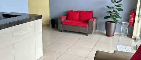 Un área de recepción con un sofá, una planta en maceta y un extintor.