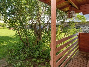 A wooden deck with a railing, surrounded by lush greenery and trees.
