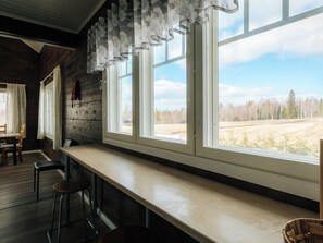 A room with a long bench, a table, and a view of a field through large windows.