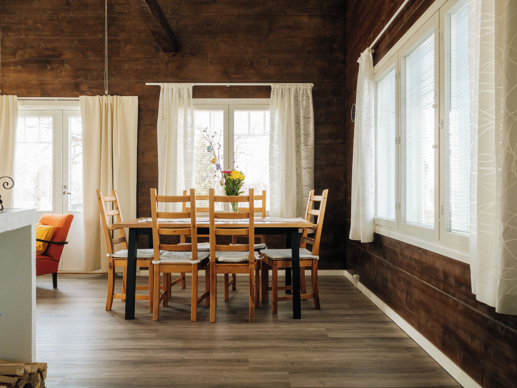Un comedor con una mesa y sillas de madera, un jarrón con flores y una ventana con cortinas.