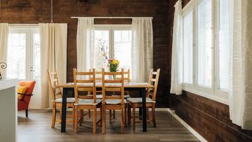 Un comedor con una mesa y sillas de madera, un jarrón con flores y una ventana con cortinas.