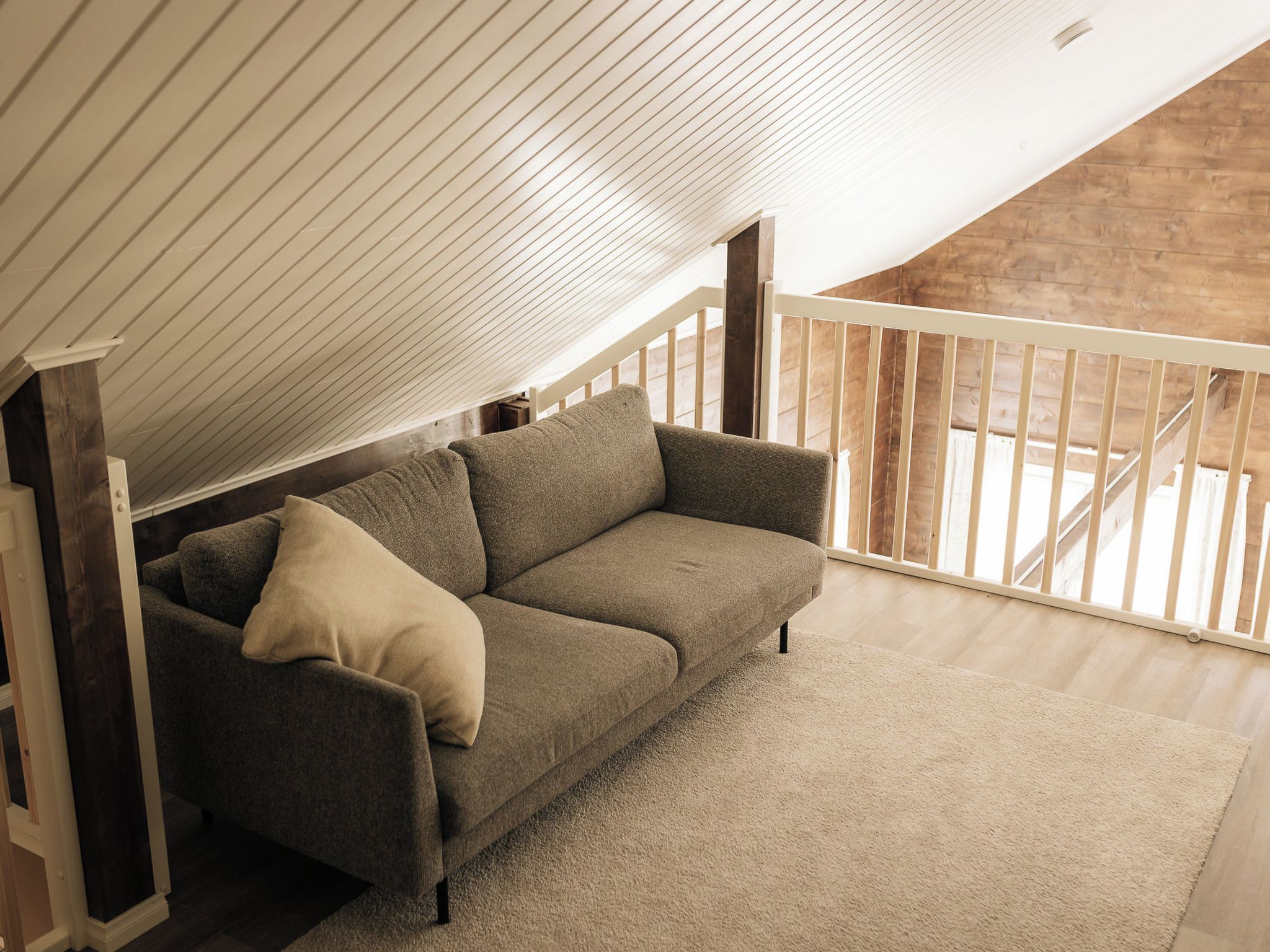 A loft-style room with a sloped ceiling, a sofa, and a view of a wooden staircase.