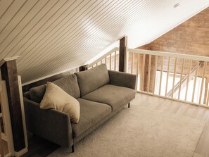 Habitación estilo loft con techo inclinado, un sofá y vistas a una escalera de madera.