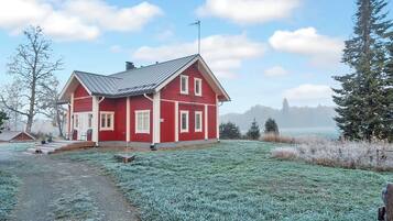 A red house with a metal roof, a wooden deck, and a view of a body of water and trees in the background.