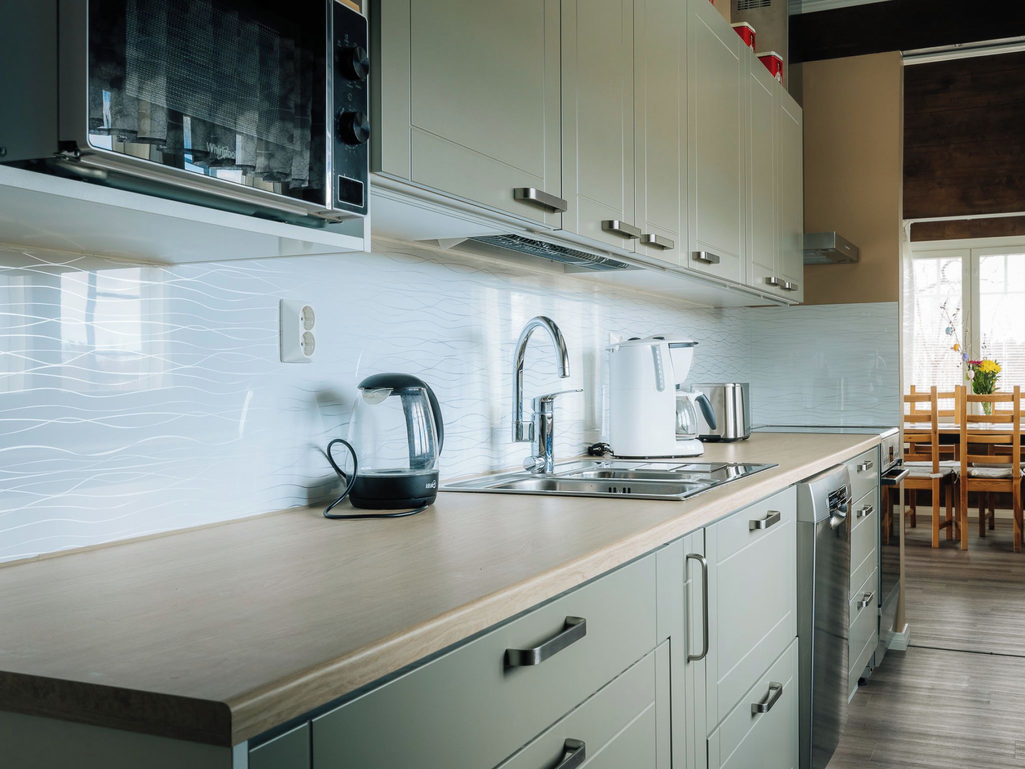 A modern kitchen with a built-in dishwasher, a kettle, and a coffee maker on the countertop.