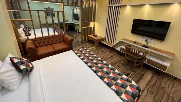 A hotel room with a bed, a sofa, a desk, a TV, and a mirror. - Forest Transit Hotel (Coimbatore)