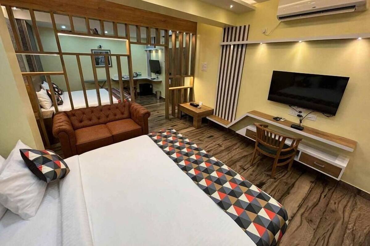 A hotel room with a bed, a sofa, a desk, a TV, and a mirror.