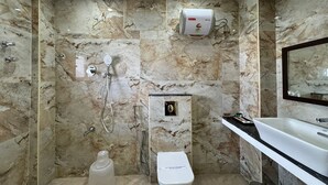 A bathroom with a marble wall, a toilet, a sink, and a shower. - Forest Transit Hotel (Coimbatore)