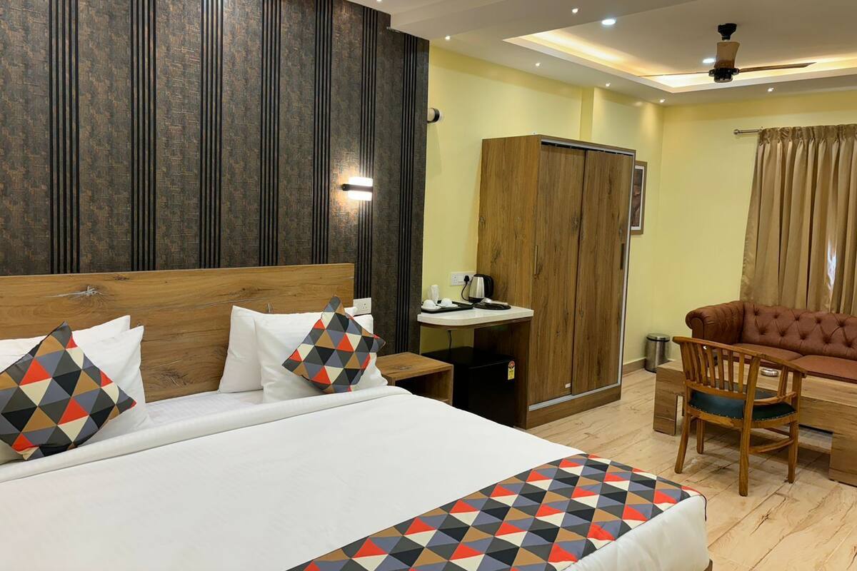 A hotel room with a large bed, a wooden wardrobe, a desk with a chair, and a sofa.