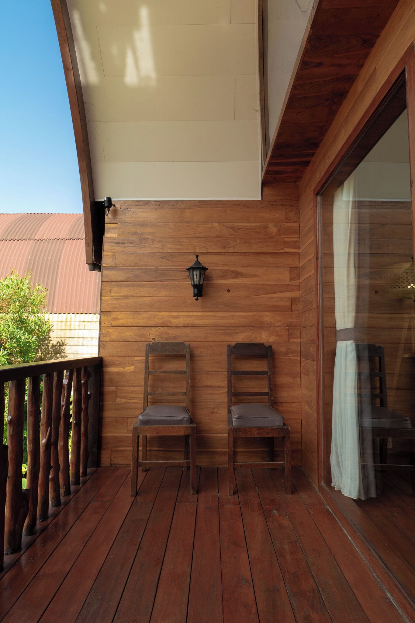 A wooden deck with two chairs and a wall-mounted light fixture.
