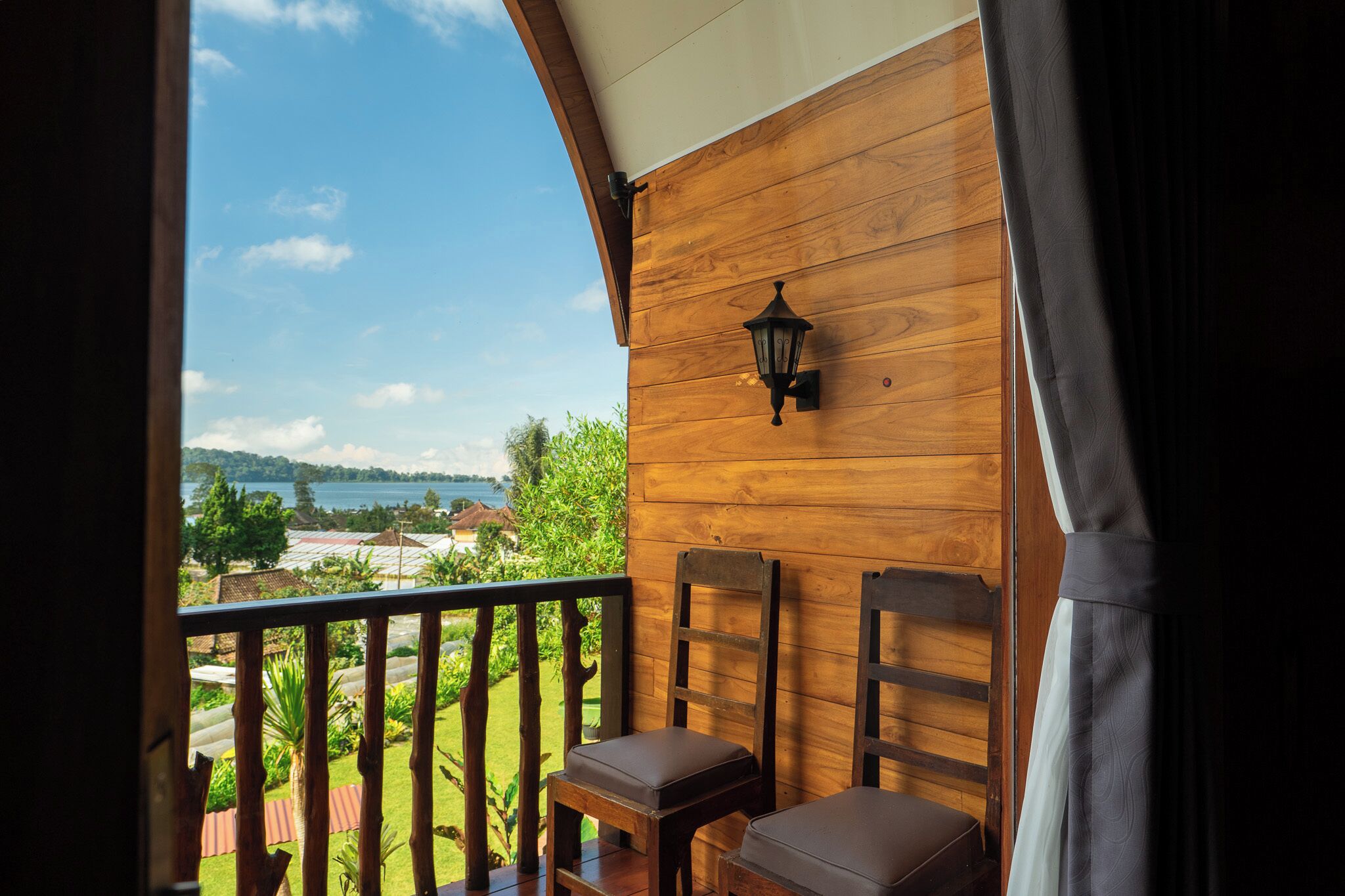 A balcony with wooden walls, a view of a lake, and two wooden chairs with cushions.