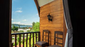A balcony with wooden walls, a view of a lake, and two wooden chairs with cushions.