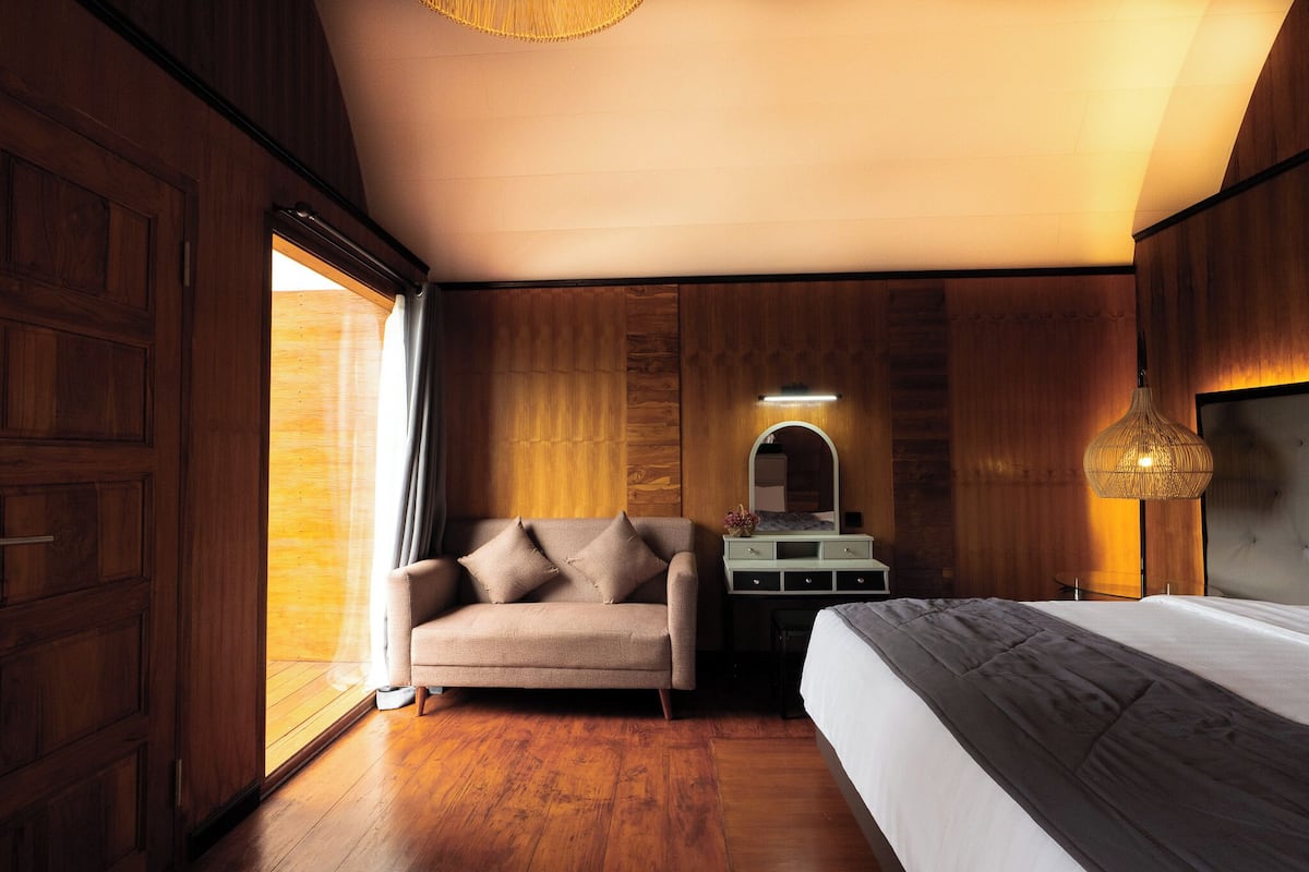 A bedroom with a wooden floor, a bed, a sofa, a dresser, and a mirror.