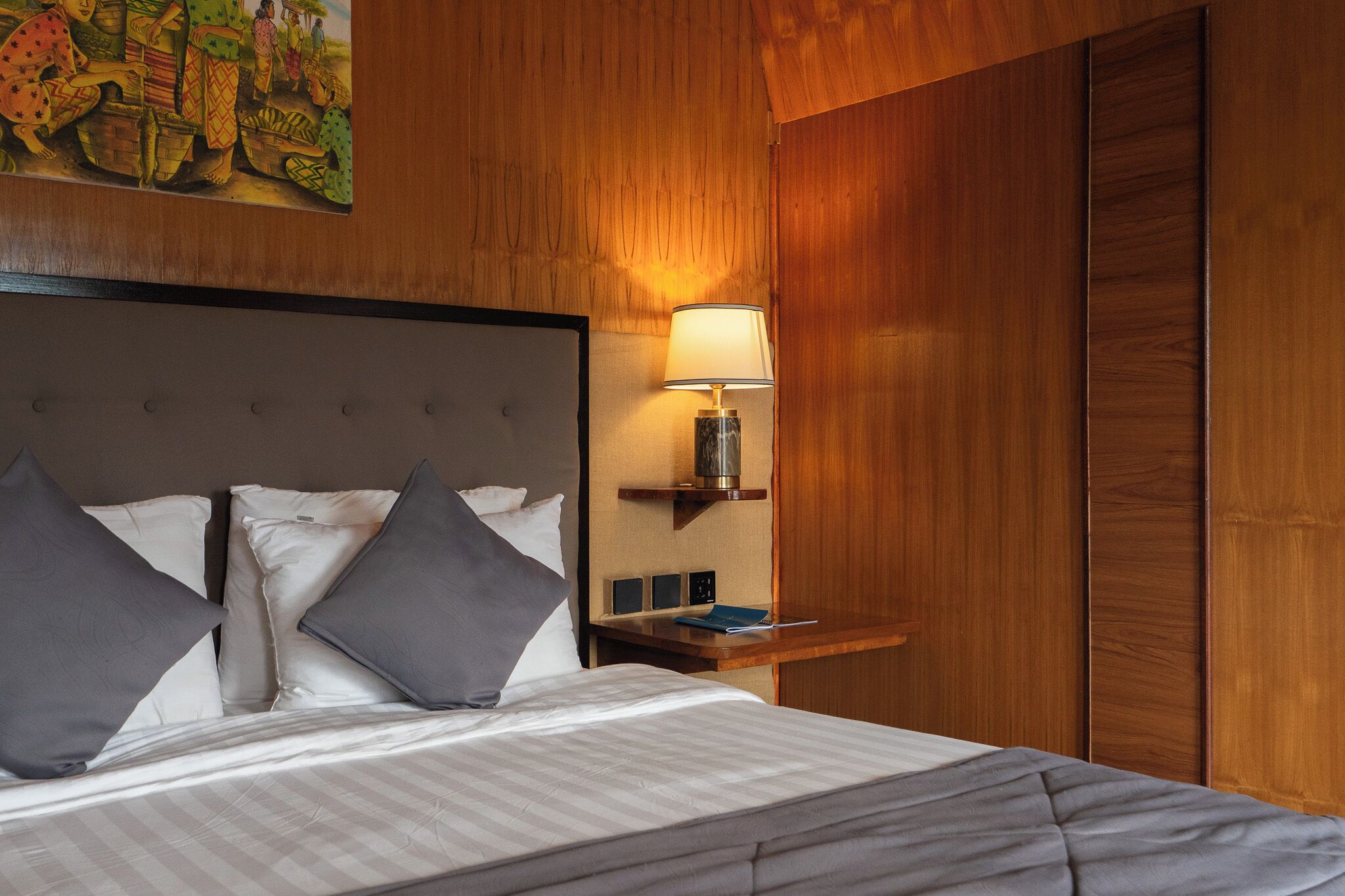 A neatly made bed with a headboard, a bedside table with a lamp, and a wooden wall panel.