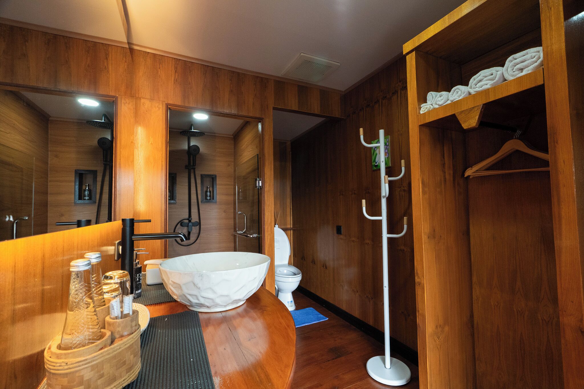 A wooden-finished bathroom with a large white basin, a towel rack, and a mirror.