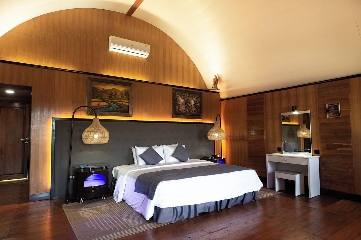 A modern bedroom with a large bed, bedside lamps, a vanity, and a painting on the wall.