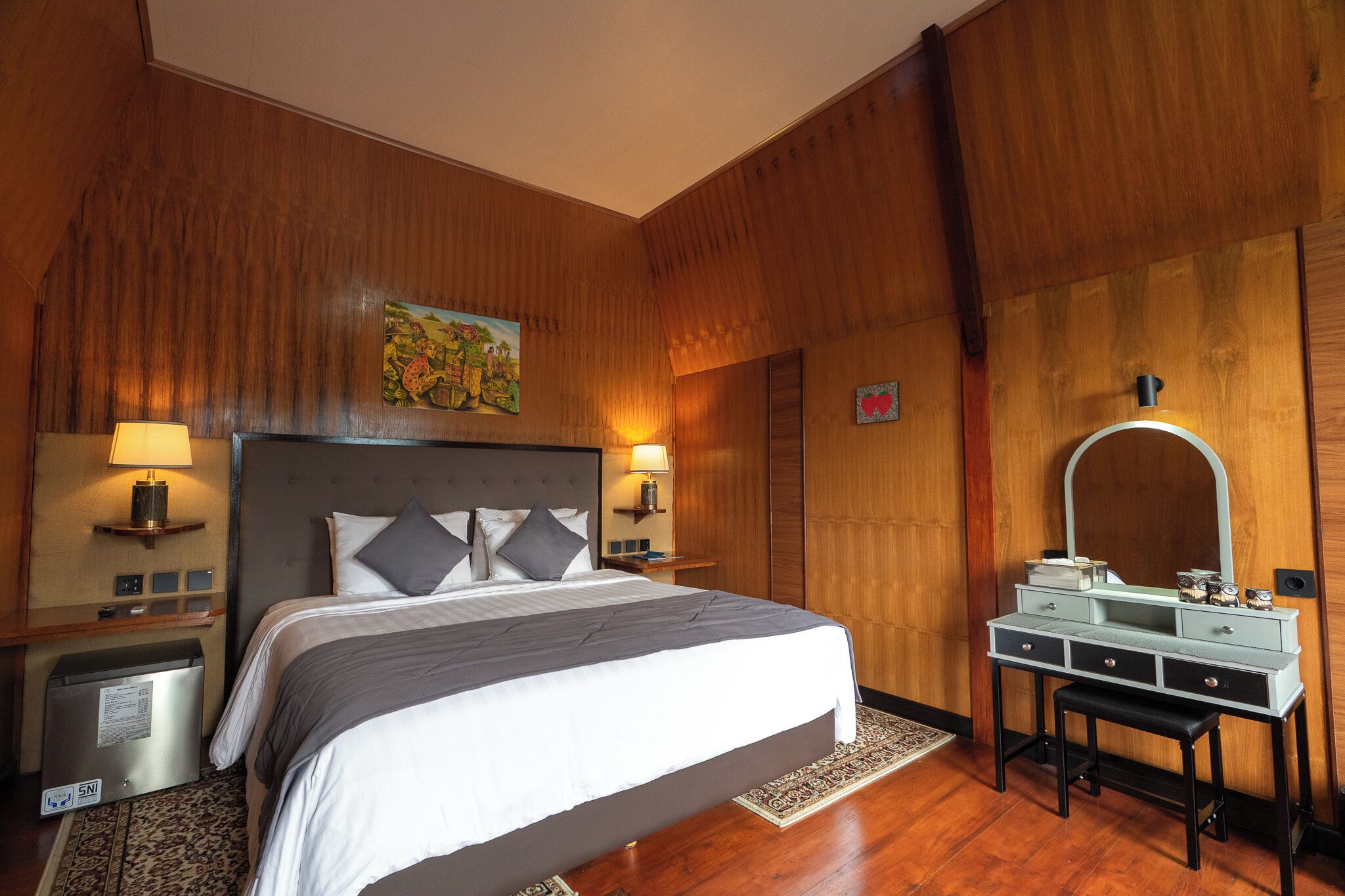 A hotel room with a large bed, bedside lamps, a dresser with a mirror, and a wooden wall panel.