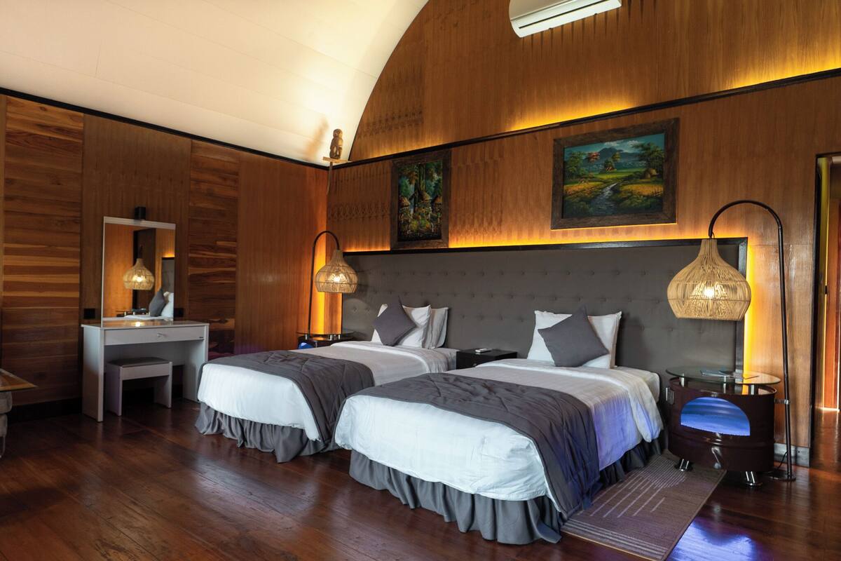 A hotel room with two beds, a desk, and a large mirror. There are wall-mounted lamps and a painting above the beds.
