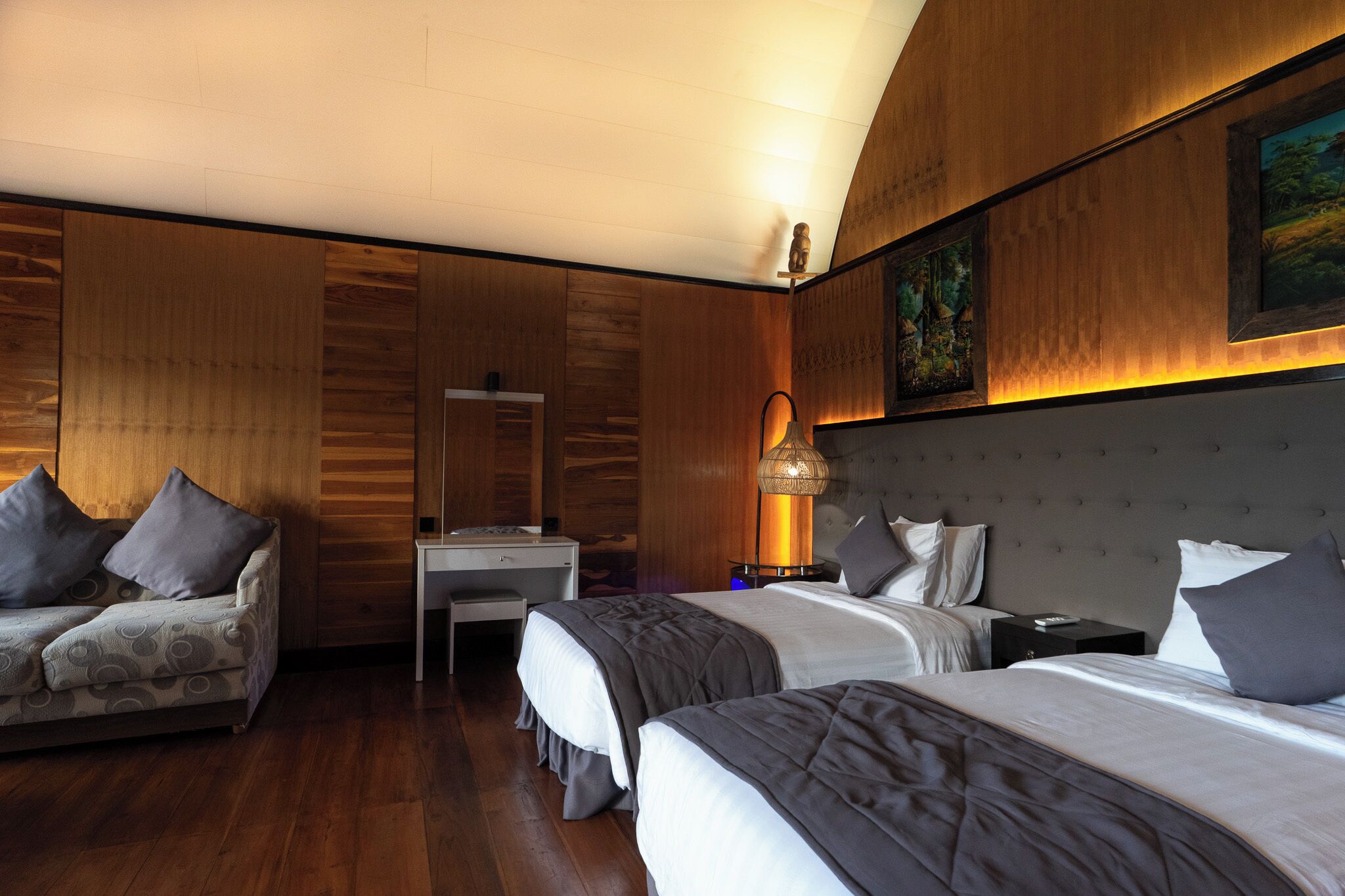 A hotel room with two beds, a desk, a sofa, and wooden paneling.