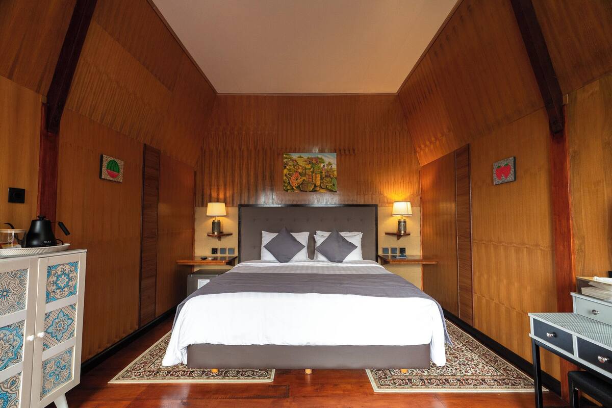 A bedroom with a large bed, wooden walls, two bedside tables with lamps, and a decorative painting above the bed.