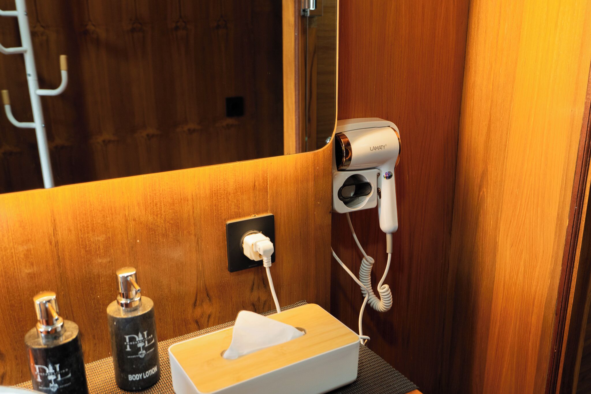 Une salle de bain équipée d’un sèche-cheveux fixé au mur, d’une boîte de mouchoirs et de deux flacons de lotion pour le corps.