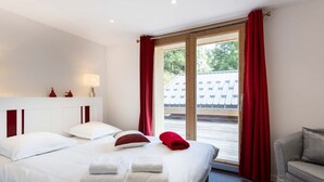 Une chambre d’hôtel avec un grand lit, un canapé, une fenêtre avec des rideaux rouges et une vue sur un immeuble.