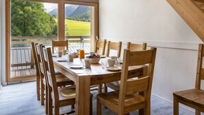 Un coin repas avec une table et des chaises en bois, de grandes fenêtres donnant sur un paysage verdoyant et des montagnes.