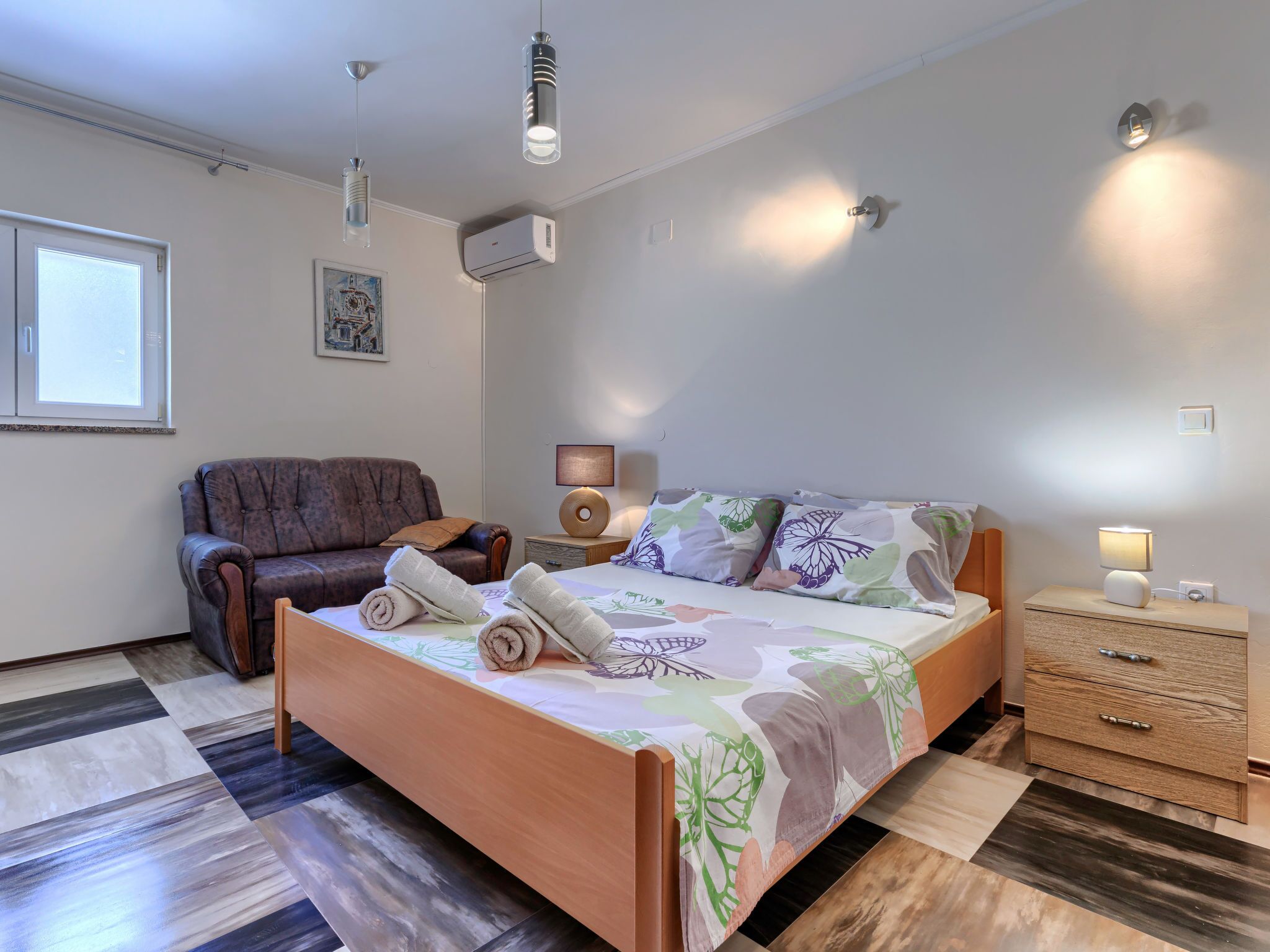 Une chambre à coucher comprenant un lit, une chaise, une table de chevet avec une lampe et un appareil de climatisation.