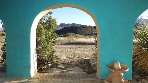 Een pad van stenen leidt door een turquoise boogpoort naar een bergachtig landschap.