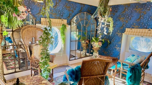 A room with wicker furniture, hanging plants, and a large window with a view. - Le Jardin Perché: Suite for Two (MOULEYDIER)