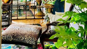 A room with a blue patterned wall, a wrought iron gate, a leopard print bench, and various potted plants. - Le Jardin Perché: Suite for Two (MOULEYDIER)