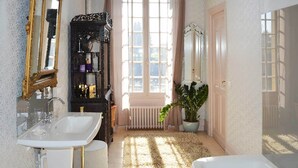 A bathroom with a white sink, a bathtub, and a large mirror with an ornate frame. There is a window with curtains, a radiator, and a potted plant. - Bed and Breakfast for Two (MOULEYDIER)