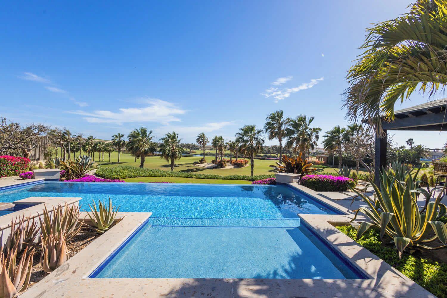 A pool with a clear view of a golf course and palm trees in the background.