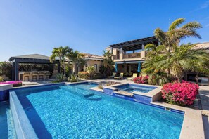 Una piscina con área de bar, palmeras y un edificio de dos pisos con balcones.