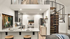A modern kitchen with a central island, a staircase, and a living area with a sofa. - Stylish Oak Creek Home w/ 2 Suites, Spa & Firepit (Sedona)