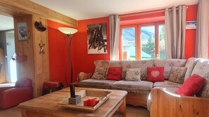 A cozy living room with a wooden sofa, a coffee table, and a large window with curtains.