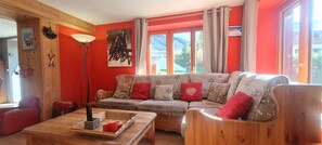 Un salon chaleureux avec un canapé en bois, une table basse et une grande fenêtre agrémentée de rideaux.