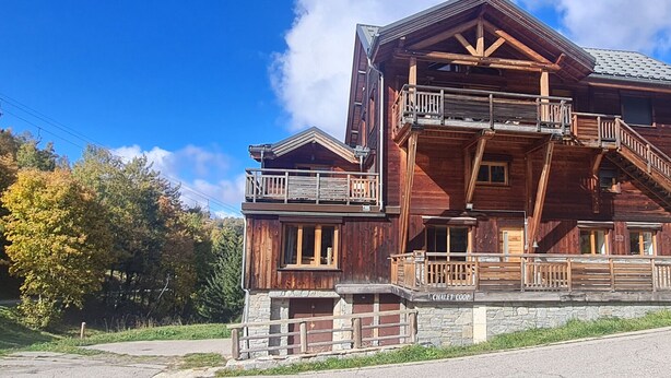 A wooden chalet with a stone foundation, multiple balconies, and a ski lift in the background.