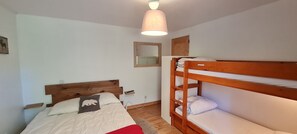 A bedroom with a wooden bunk bed, a single bed with a headboard, a bedside table, a mirror, and a hanging light fixture. - Nice Apt 6 pers in Chalet (Les Deux Alpes)