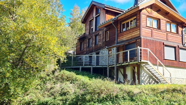 A wooden chalet with a stone base, a balcony, and a staircase leading to the upper floor.