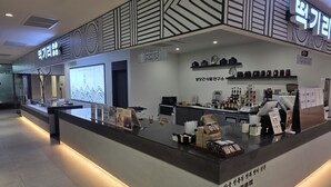 A modern cafe with a minimalist design, featuring a counter with various items for sale and a display of coffee machines. - villiv Inn The City Namsan (Seoul)