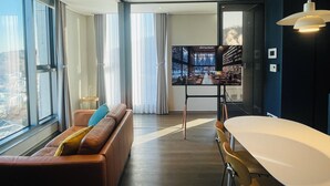 A modern hotel room with a large window, a sofa, a dining table, and a view of a cityscape. - villiv Inn The City Namsan (Seoul)