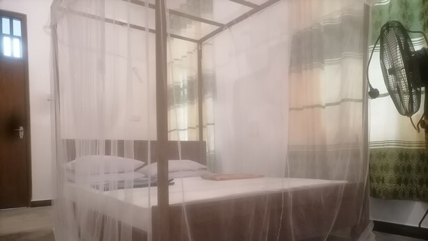A bed with a canopy, a wooden door, and a wall-mounted fan. - Hasmal house hiriketiya (Dikwella)