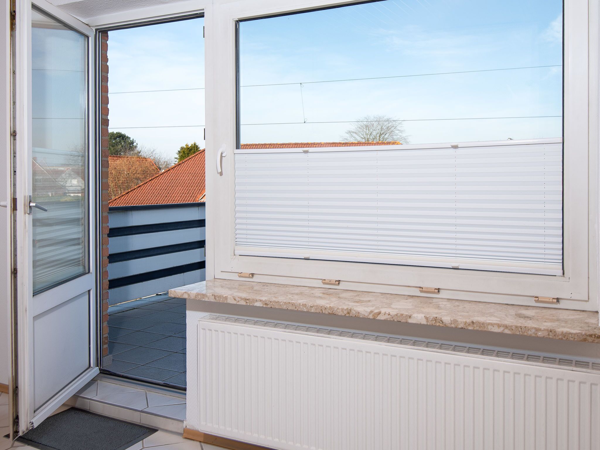 Een kamer met een schuifdeur, een radiator en uitzicht op een aangrenzend gebouw met een pannendak.